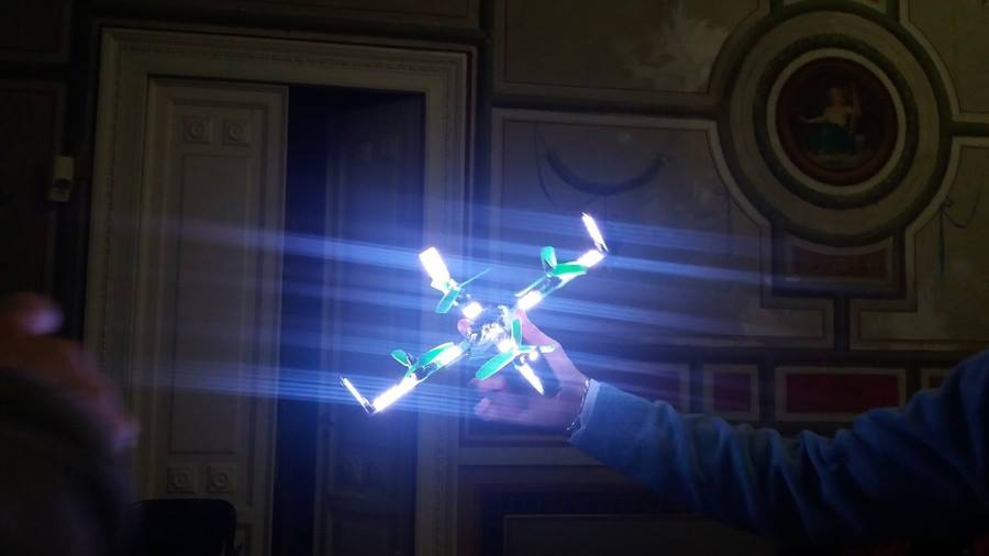 First LuminousBee prototype glowing with bright LEDs, held up at the press conference in a historic Italian room